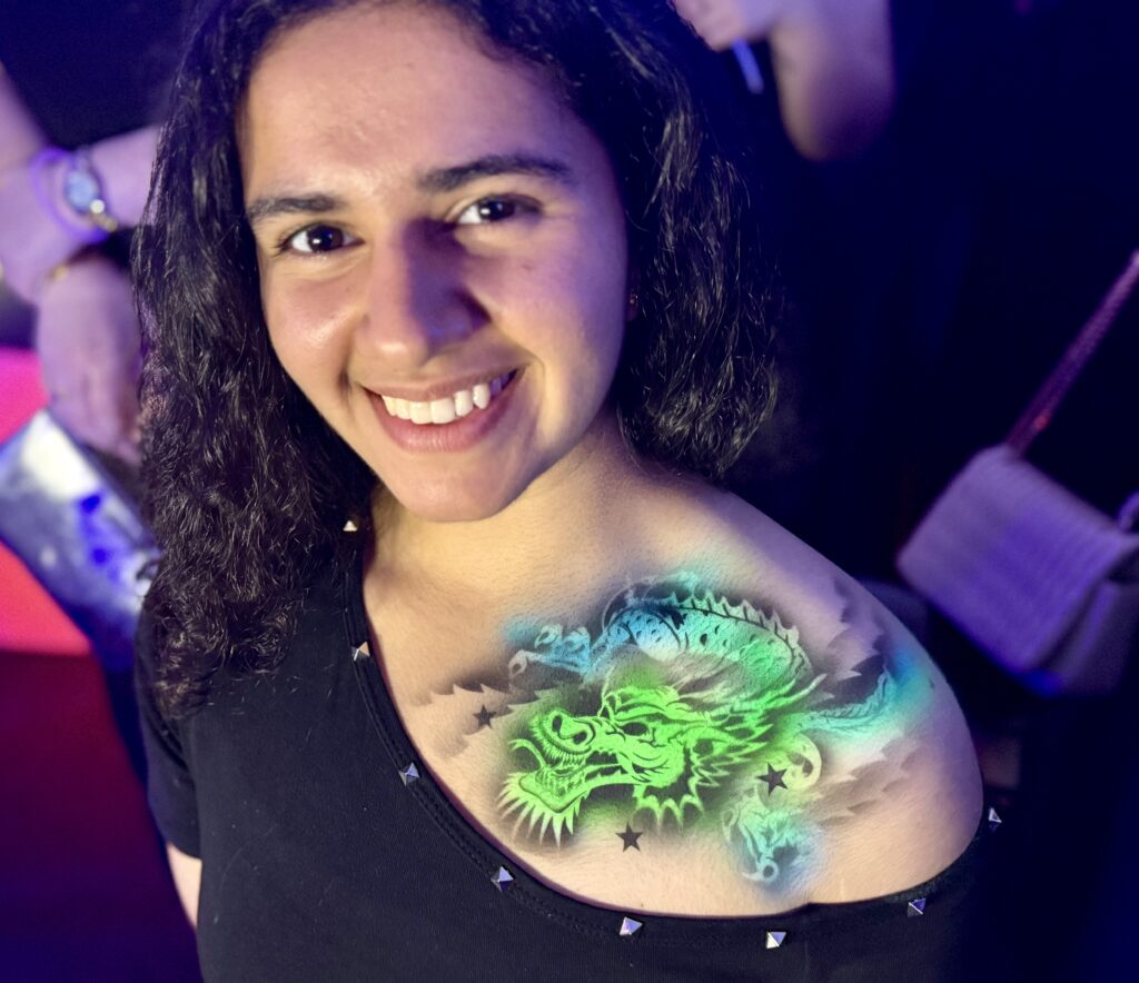 Woman wearing a colourful UV airbrush dragon body art design across her shoulder and chest